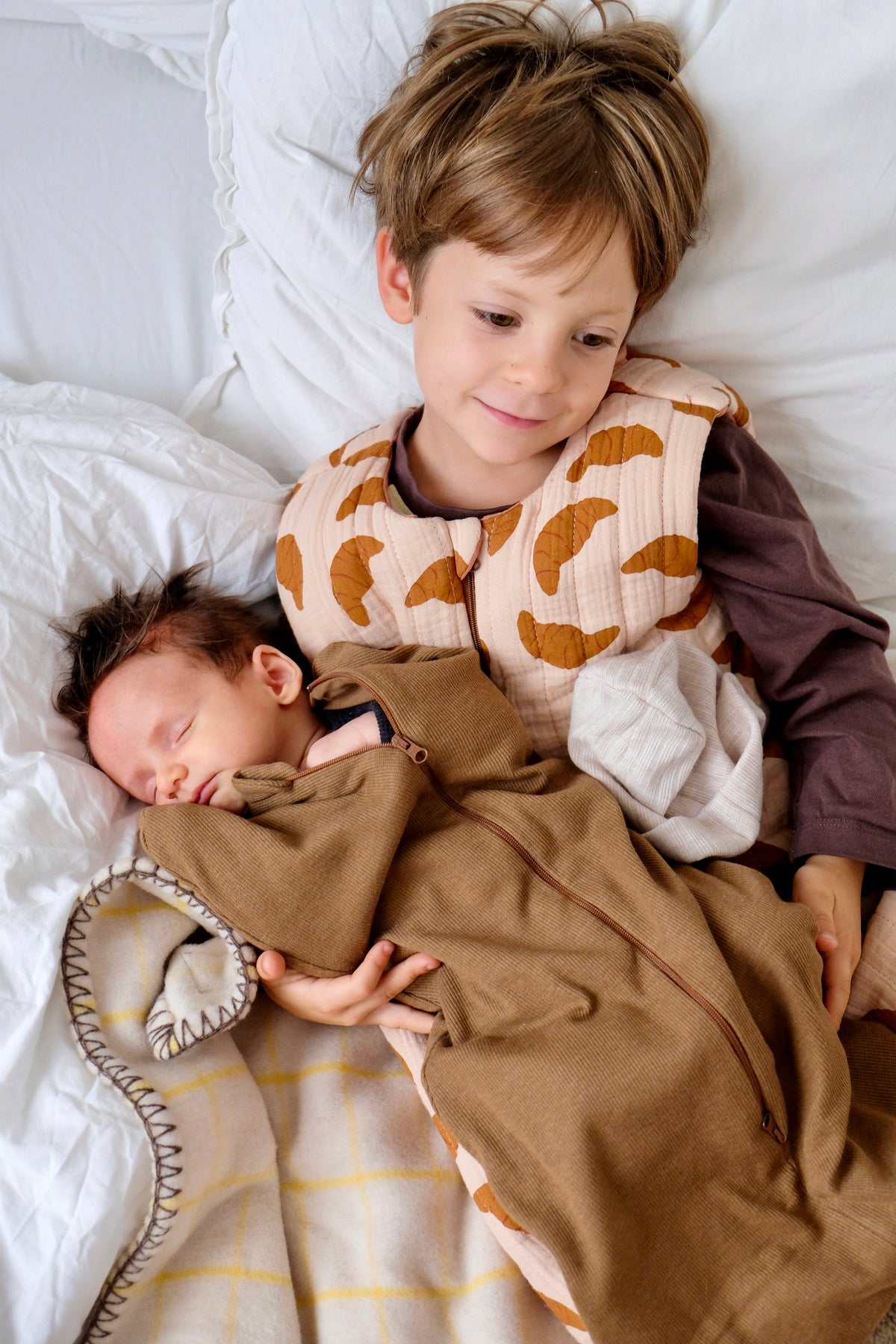 bebe emmaillote et son grand frere sur un lit