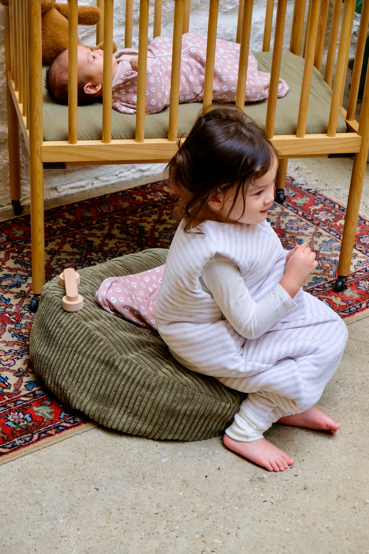 soeurs dont une allongée dans une emmailloteuses sur lit barreau et l'autre en gigoteuse à pieds sur nid bag matcha